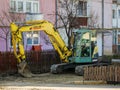 Excavator on road construction site in front of an old apartment building.