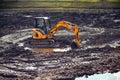 An excavator is standing in the mud. Cleaning the drained pond from dirt and debris