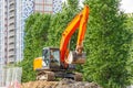 An excavator stands on heaps of soil during the construction of the road against the background of trees