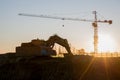 Excavator and tower crane at construction site on sunset background. Construction crane constructing a new building Royalty Free Stock Photo