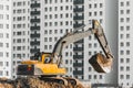 Excavator work on the ground on background of multi storey houses.