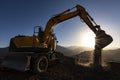 Excavator is working on the hill at sunset. Excavators are heavy construction equipment consisting of a boom, dipper or stick, b