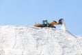 Excavator working in a huge pile salt at saltworks. Marine salt produced by the evaporation of seawater