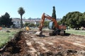 construction site with an orange excavator digging soil in an urban park area surrounded by trees and residential buildings Royalty Free Stock Photo