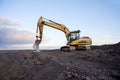 Excavator working at open pit mining on sunset background. Backhoe digs gravel in sand quarry on blue sky background