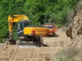 An excavator works on a mountain road repair on a sunny summer day Royalty Free Stock Photo