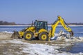 Excavator works on the rivershore. Cleaning shore of ice and snow Royalty Free Stock Photo