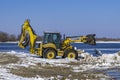 Excavator works on the rivershore. Cleaning shore of ice and snow Royalty Free Stock Photo