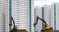 Excavators work on the sand on the background of multi-storey houses.