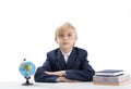 Excellent boy sits at table with his hands folded and stares seriously at camera. Bright student next to notebooks and globe Royalty Free Stock Photo