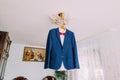 Excellent expensive blue suit with red bow-tie hanging on luster