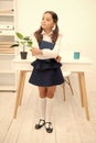 Excellent first former. Girl child hold book while stand table white interior. Kid school uniform happy face hold book