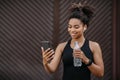 Excellent result. Girl with wireless headphones and fitness tracker holds bottle and looks at smartphone