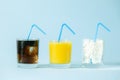 Excessive sugar consumption concept - cola, juice and sugar cubes in glasses on blue background