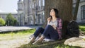 Exchange student sitting under tree, holding notebook, thinking on project