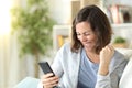 Excited adult woman celebrating news on phone at home