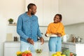 Excited african american couple cooking together, preparing fresh vegetable salad for dinner in kitchen at home Royalty Free Stock Photo