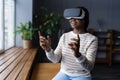 Excited black woman wear vr headset goggles play virtual reality video game in glasses alone at home