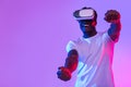 Excited African American guy in VR headset playing online game in virtual reality, driving imaginary car in neon light