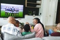 Excited african american parents, son, daughter and grandparents watching rugby on tv, slow motion