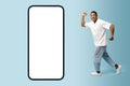 Excited African-American young man running towards to huge smartphone with empty blank mobile screen