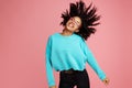 Excited african american young woman with bright smile dressed in casual clothes, glasses and headphones dance over pink