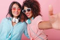 Excited african girl with red manicure making selfie with hispanic female friend. Fashionable latin woman in pink Royalty Free Stock Photo