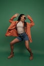 Excited african girl in shorts and shirt dancing, having fun isolated on dark green background. Concept of beauty, art Royalty Free Stock Photo