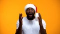 Excited Afro-American man in Santa hat, Christmas magic, yellow background