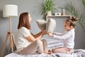 Excited amazed family mother and daughter having fun together playing fighting with pillows laughing sitting on bedroom on bed Royalty Free Stock Photo