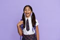 Excited amazed indian school girl holds backpack isolated on violet background.