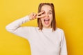 Excited amazed teenage girl in jumper with ponytails isolated over yellow background celebrating her victory success showing v Royalty Free Stock Photo