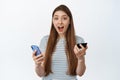 Excited and amazed young woman holding credit card and mobile phone, surprised reaction to special offer, discount at Royalty Free Stock Photo