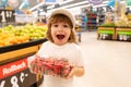Excited american kid with shopping trolley with in grocery store. Little boy in the supermarket holdind strawberry. Royalty Free Stock Photo