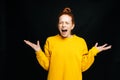 Excited angry young woman in yellow sweater screaming with closed eyes on isolated black background Royalty Free Stock Photo