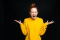 Excited angry young woman in yellow sweater screaming with closed eyes on isolated black background