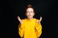 Excited angry young woman in yellow sweater screaming with closed eyes on isolated black background