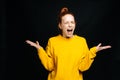 Excited angry young woman in yellow sweater screaming with closed eyes on isolated black background Royalty Free Stock Photo