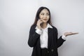Excited Asian businesswoman wearing black suit pointing at the copy space beside her while talking on her phone, isolated by white Royalty Free Stock Photo