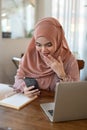 An excited Asian-Muslim woman is looking at her smartphone screen with a surprising face Royalty Free Stock Photo