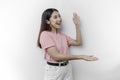 Excited Asian woman is wearing pink t-shirt, pointing at the copy space beside her, isolated by white background Royalty Free Stock Photo