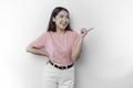 Excited Asian woman is wearing pink t-shirt, pointing at the copy space beside her, isolated by white background Royalty Free Stock Photo