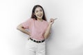 Excited Asian woman is wearing pink t-shirt, pointing at the copy space beside her, isolated by white background Royalty Free Stock Photo