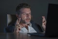 Excited and attractive businessman crossing fingers for luck hoping to win online bet while working late night at office laptop