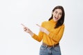 Excited attractive caucasian woman pointing fingers left, showing advertisement and inviting to check it out. Girl with Royalty Free Stock Photo