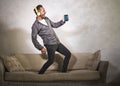 Excited attractive man listening online music with headphones and mobile phone singing song and dancing carefree jumping at Royalty Free Stock Photo