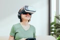 Excited attractive woman gaming with virtual reality headset or goggles and sitting on the couch, holding gamepad controller and