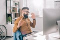 Excited bearded adult businessman in earphones sitting at computer and listening to music desk