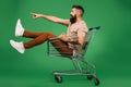 Excited bearded man showing something while sitting in shopping cart isolated