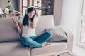 Excited beautiful brunette teen is listening to music in big white earphones at home. She is wearing casual clothes, sitting on c Royalty Free Stock Photo